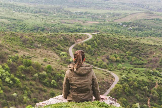 vlad-bagacian-d1eaoAabeXs-unsplash A women sitting on top of a hill looking down on the winding path below.